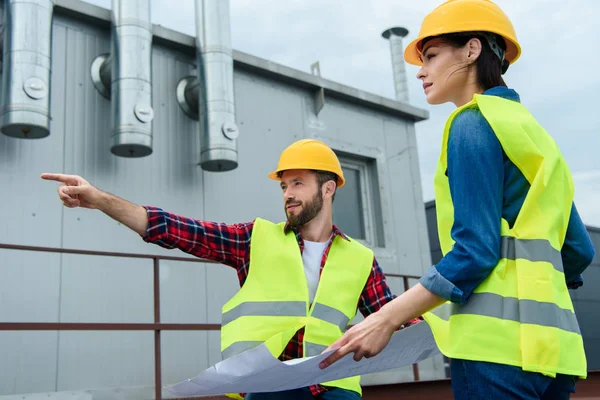 Arquitectos profesionales en cascos que trabajan con planos y gestos en la construcción - foto de stock