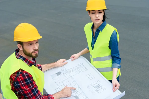 Ingenieros profesionales en sombreros de trabajo con planos en el techo - foto de stock