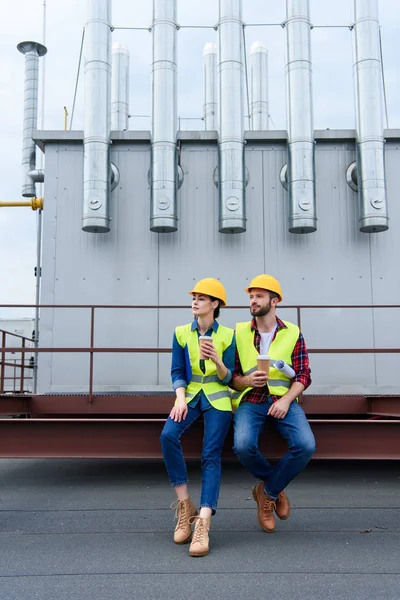 Male and female engineers in helmets with blueprint on coffee break sitting on roof — Stock Photo