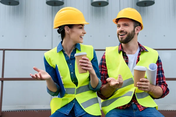 Engineers in helmets with blueprint on coffee break sitting on roof — Stock Photo