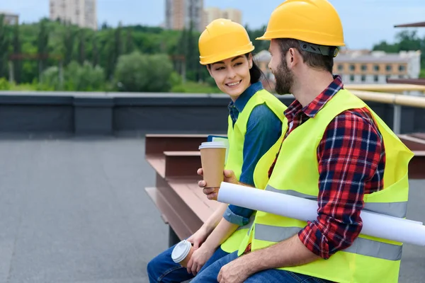 Architetti in casco con cianografia sulla pausa caffè seduti sul tetto — Foto stock