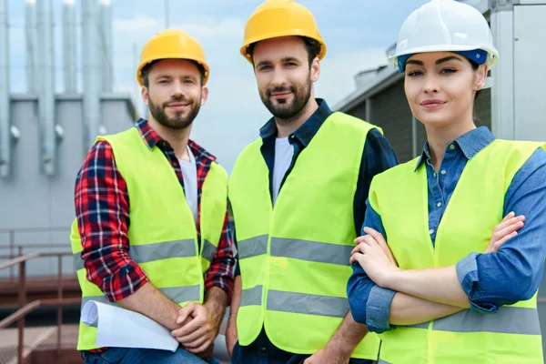 Professional engineers in safety vests and hardhats posing with crossed arms — Stock Photo