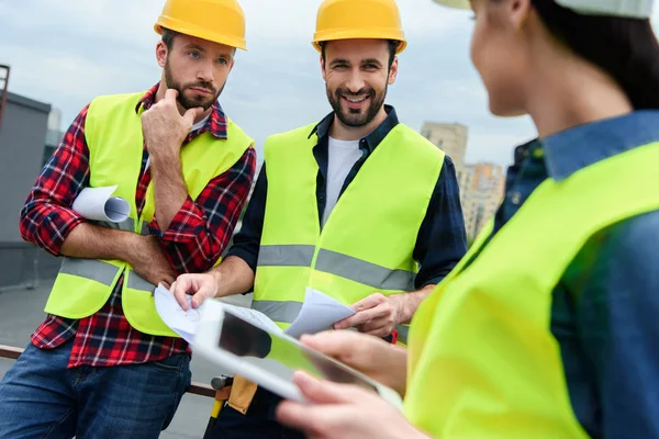 Ingenieros en chalecos de seguridad y sombreros de trabajo con tableta digital y planos - foto de stock