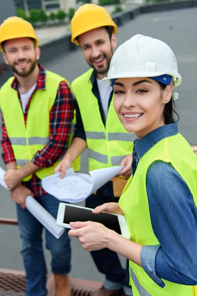 Architects in safety vests and hardhats working with digital tablet and blueprints — Stock Photo