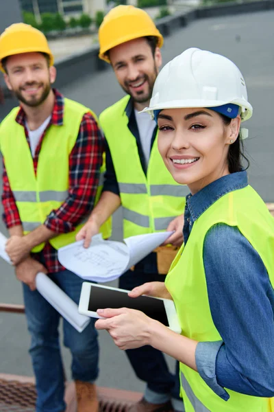 Arquitetos em coletes de segurança e hardhats trabalhando com tablet digital e plantas — Fotografia de Stock