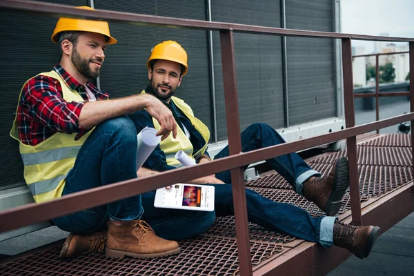 Arquitetos com plantas e tablet digital com site soundcloud sentado em construção — Fotografia de Stock