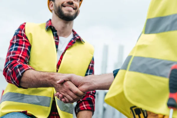Cropped view of engineers in safety vests shaking hands on roof — Stock Photo