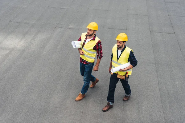 Overhead view of architects in safety vests and hardhats with blueprints — Stock Photo