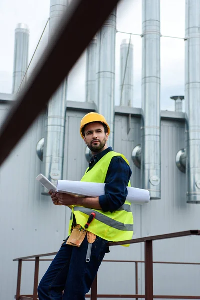 Engenheiro masculino em colete de segurança e capacete com planta usando tablet digital na construção — Fotografia de Stock