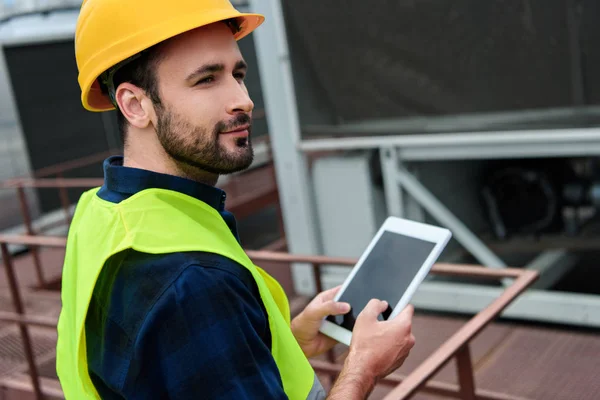 Arquitecto en chaleco de seguridad y casco usando tableta digital con pantalla en blanco - foto de stock