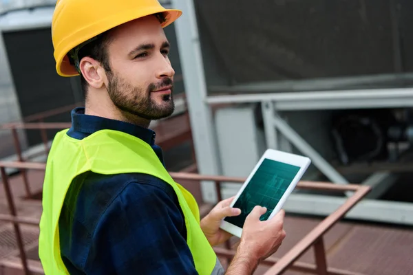 Ingegnere maschio in giubbotto di sicurezza e casco utilizzando tablet digitale con grafici — Foto stock