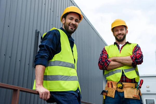 Deux architectes en gilets de sécurité et casques de sécurité debout sur la construction — Photo de stock