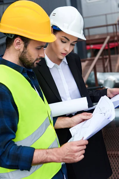 Female engineer and male worker looking at blueprints on construction — Stock Photo
