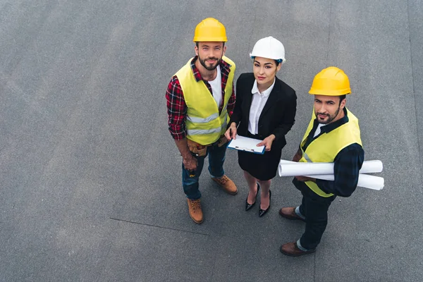 Overhead-Ansicht von Ingenieurinnen und männlichen Arbeitern mit Clipboard und Bauplänen — Stockfoto