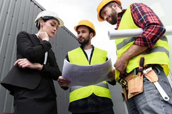 Vue du bas de l'ingénieur féminin et des travailleurs masculins avec des plans sur la construction — Photo de stock