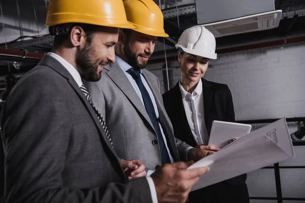 Engineers in suits and hardhats working with blueprint and digital tablet on construction — Stock Photo