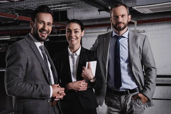 Hombres de negocios sonrientes y mujer de negocios con tableta digital posando en trajes juntos - foto de stock