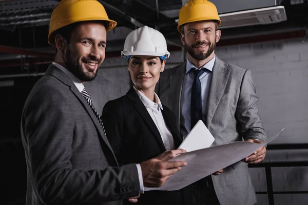 Architects in suits and helmets working with blueprint and digital tablet on construction together — Stock Photo
