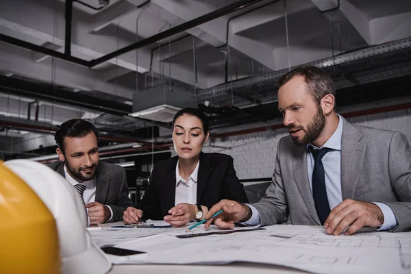 Architects and engineers in suits working at table with blueprints and hardhats — Stock Photo