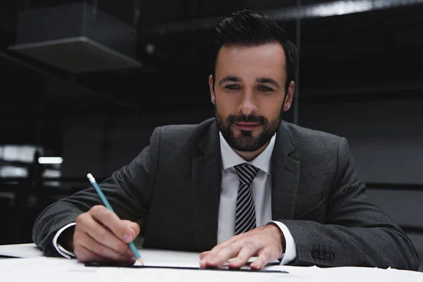 Hombre de negocios sonriente trabajando con planos y lápiz - foto de stock