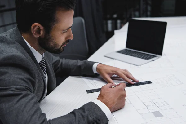 Architecte masculin fatigué travaillant avec des plans et un ordinateur portable — Photo de stock