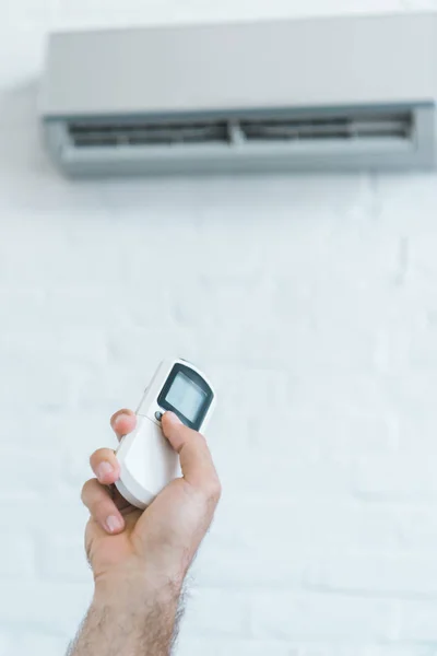 Cropped view of man turning on air conditioner with remote control — Stock Photo
