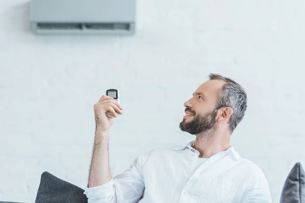 Hombre barbudo encendiendo el aire acondicionado con control remoto - foto de stock