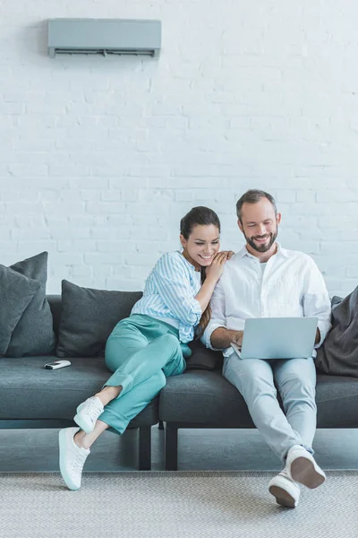 Paar mit Laptop auf dem Sofa während der Sommerhitze mit Klimaanlage an der Wand — Stockfoto