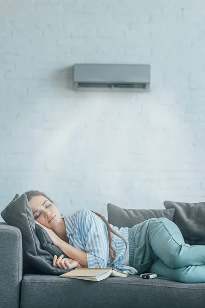 Femme dormir sur canapé avec livre et climatiseur soufflant sur elle — Photo de stock