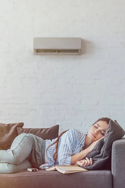 Femme dormir sur canapé avec livre et climatiseur sur le mur — Photo de stock