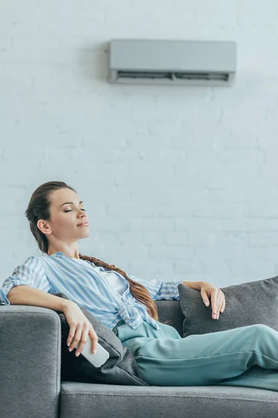 Mulher descansando no sofá com ar condicionado na parede, conceito de calor de verão — Fotografia de Stock