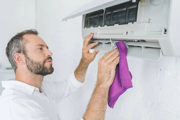 Bärtiger Mann reinigt Klimaanlage mit Lappen — Stockfoto