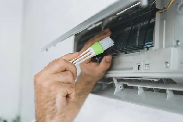 Ausgeschnittene Ansicht eines männlichen Arbeiters, der Klimaanlage mit Pinsel reinigt — Stockfoto