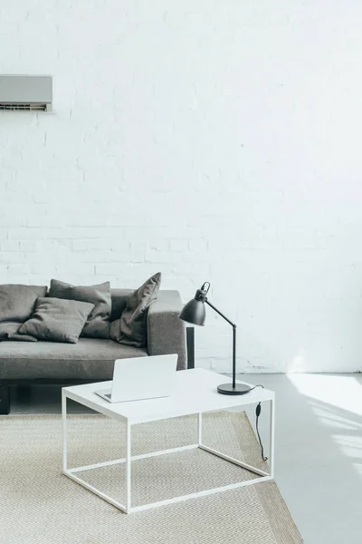 Chambre avec canapé gris, lampe et ordinateur portable sur la table et climatiseur au mur — Photo de stock
