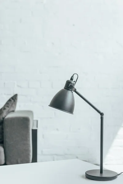 Lámpara negra de pie sobre la mesa en la habitación con sofá gris - foto de stock