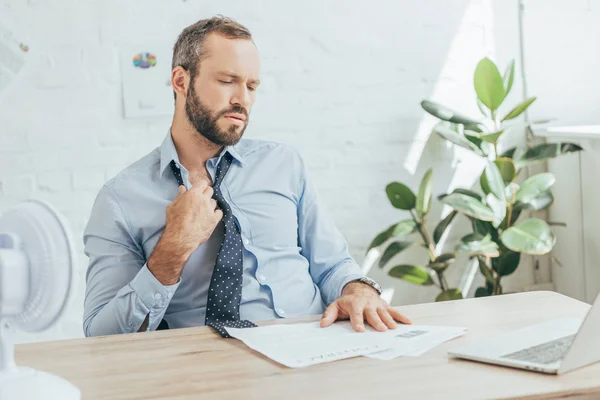 Hombre de negocios aire acondicionado con ventilador eléctrico en oficina con papeleo - foto de stock