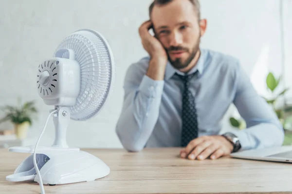 Enfoque selectivo de hombre de negocios en la oficina con ventilador eléctrico blanco - foto de stock