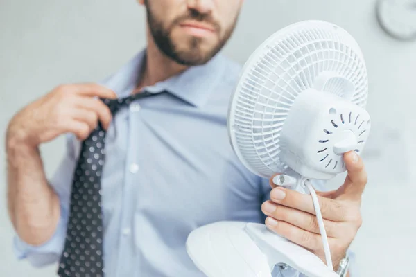 Обрезанный вид бизнесмена, охлаждающего себя электрическим вентилятором — стоковое фото