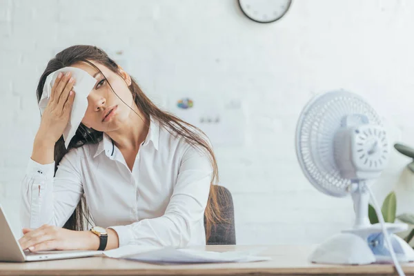 Mujer de negocios sudorosa trabajando en la oficina con ventilador eléctrico - foto de stock