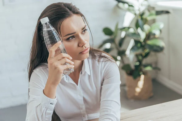 Upset businesswoman cooling herself with cold bottle of water in hot office — Stock Photo