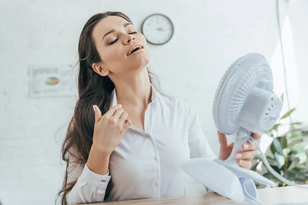 Mujer de negocios acondicionándose con ventilador eléctrico en la oficina - foto de stock