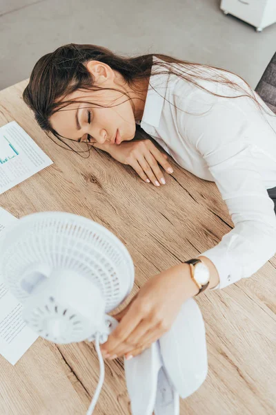 Exhausted businesswoman blowing at herself with electric fan in office — Stock Photo