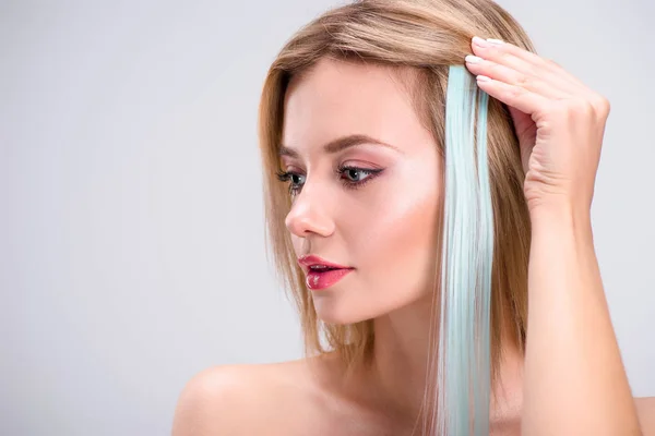 Hermosa mujer joven aplicando gris clip en hebra de pelo aislado en gris - foto de stock