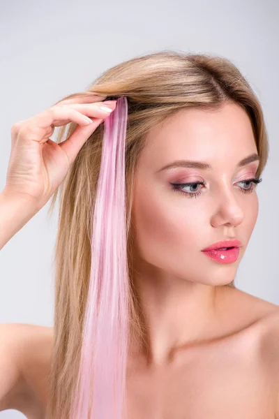 Atractiva mujer joven aplicando clip rosa en hebra de pelo aislado en gris - foto de stock