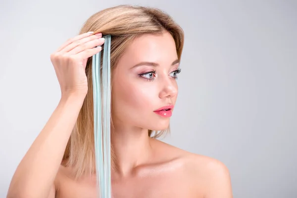 Atractiva mujer joven aplicando clip gris en hebra de pelo aislado en gris - foto de stock