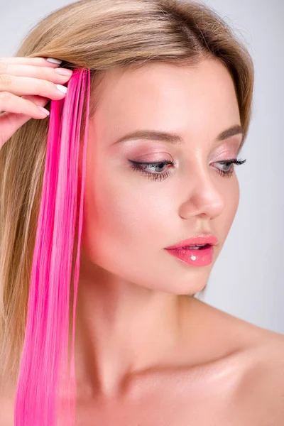 Hermosa mujer joven aplicando clip rosa en hebra de pelo aislado en gris - foto de stock