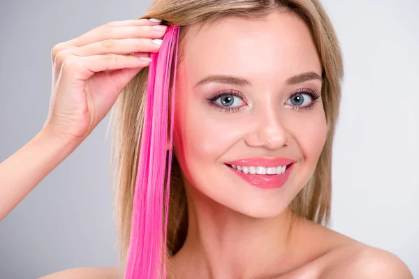 Happy young woman applying pink clip-on hair strand isolated on grey — Stock Photo