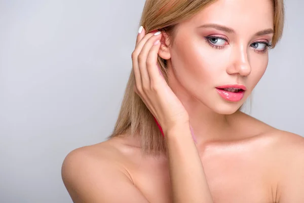 Retrato de cerca de la hermosa mujer joven poniendo pelo detrás de la oreja aislado en gris - foto de stock