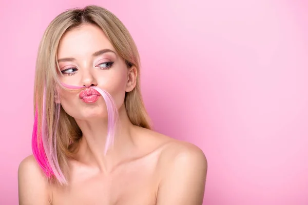 Attractive young woman making mustache with pink hair strand isolated on pink — Stock Photo