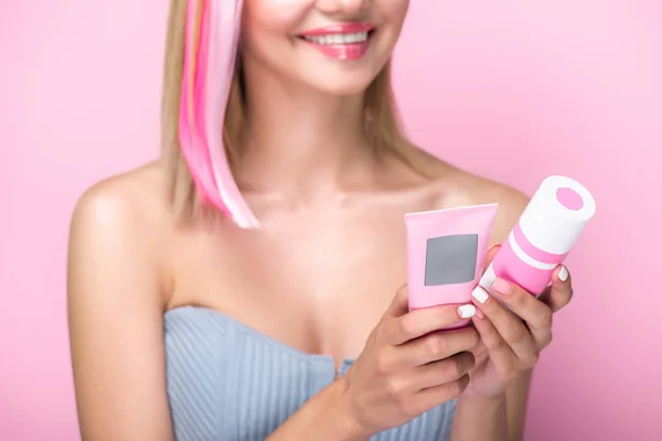 Tiro recortado de mujer joven con hebras de pelo de colores que sostienen tratamientos capilares aislados en rosa - foto de stock